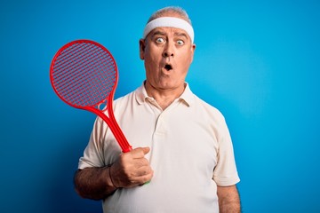 Middle age hoary sportsman playing tennis using racket over isolated blue background scared in shock with a surprise face, afraid and excited with fear expression
