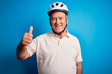 Middle age hoary cyclist man wearing bike security helmet over isolated blue background doing happy thumbs up gesture with hand. Approving expression looking at the camera showing success.