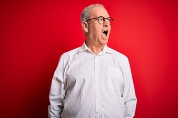 Middle age handsome hoary man wearing casual shirt and glasses over red background angry and mad screaming frustrated and furious, shouting with anger. Rage and aggressive concept.