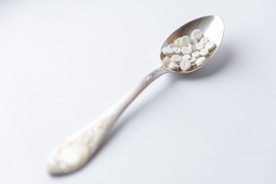 Medicine and health, treatment, pharmacy, coronavirus, pandemic, epidemic concept - layout one silver big tablespoon with different pills and capsules on a white background copy space.