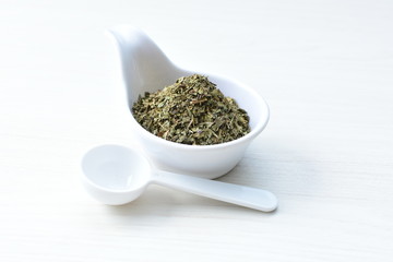 Chopped dried leaves of basil leaves on white wooden background