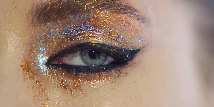 Close Up Shot Of A Blue Eye, Iris With Colorful Glittery Make Up And Black Bold Eyeliner. Party Make Up. Eye Blinks.