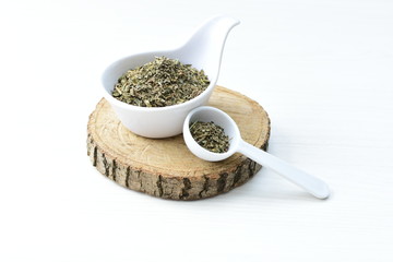 Chopped dried leaves of basil leaves on white wooden background