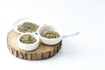 Chopped dried leaves of basil leaves on white wooden background