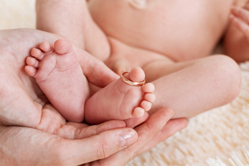 mother hold feets with gold ring of newborn baby