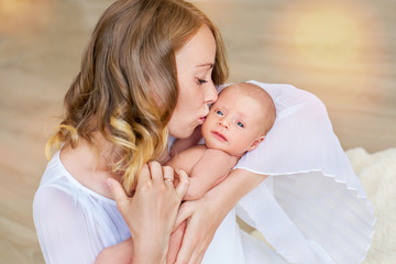 Blonde Mom holds her 2-month-old baby in her arms and smiles