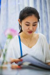 Young beautiful Asian girl customer reading the menu at the cafe, making an order at the restaurant, selective focus, blurred bokeh background, film noise grain