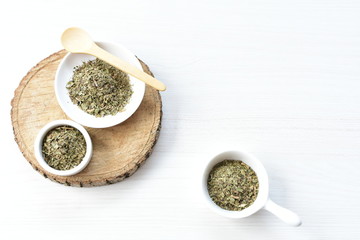 Chopped dried leaves of basil leaves on white wooden background