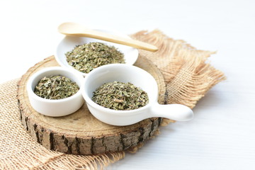 Chopped dried leaves of basil leaves on white wooden background