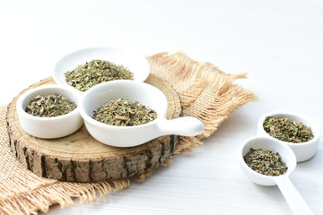 Chopped dried leaves of basil leaves on white wooden background