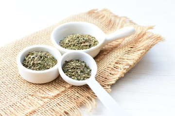 Chopped dried leaves of basil leaves on white wooden background