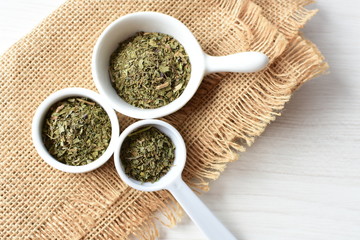 Chopped dried leaves of basil leaves on white wooden background