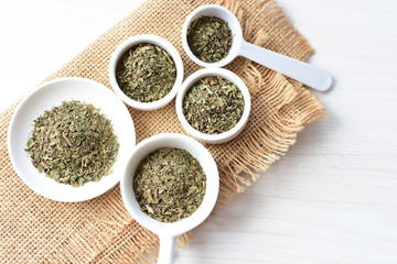 Chopped dried leaves of basil leaves on white wooden background