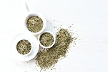 Chopped dried leaves of basil leaves on white wooden background