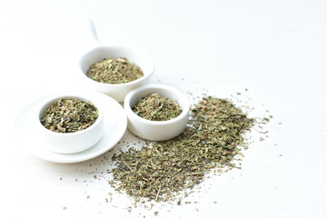Chopped dried leaves of basil leaves on white wooden background