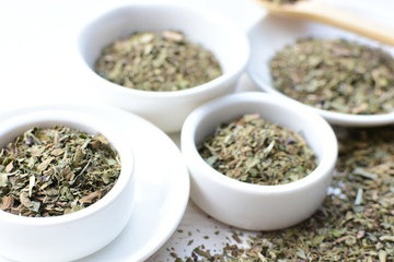 Chopped dried leaves of basil leaves on white wooden background