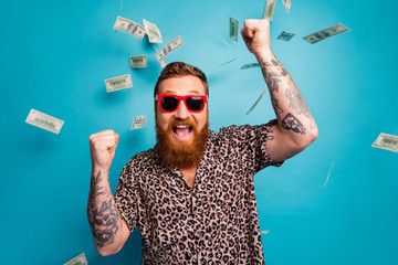 Photo of crazy handsome guy luxury rich person dollars fall from sky lottery cashback open mouth win big money raise fists wear leopard shirt sun specs isolated blue background