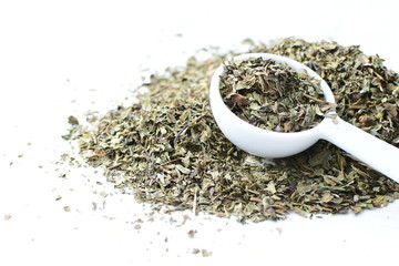 Chopped dried leaves of basil leaves on white wooden background