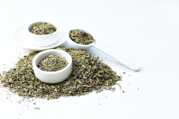 Chopped dried leaves of basil leaves on white wooden background
