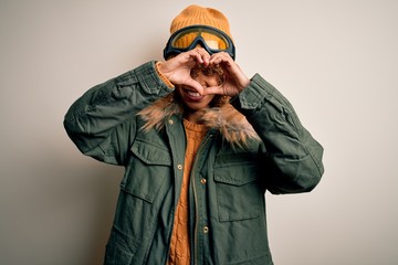 Young african american skier woman with curly hair wearing snow sportswear and ski goggles Doing heart shape with hand and fingers smiling looking through sign