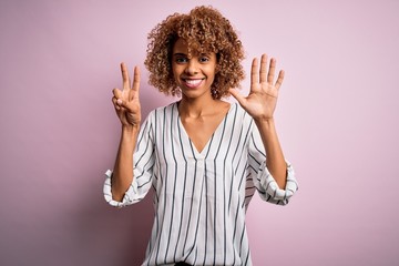 Beautiful african american woman with curly hair wearing striped t-shirt over pink background...
