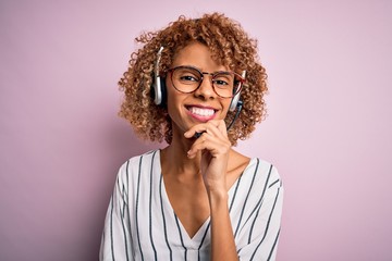 African american curly call center agent woman working using headset over pink background looking...