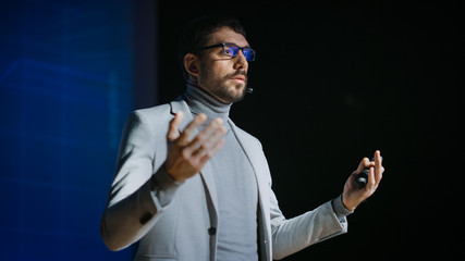 Great Motivational Speaker Stands on Stage, Talks about Happiness, Self, Success, Technology and How To Be Productive. Startup Presenter Pitching Ideas. Cinematographic Photo.