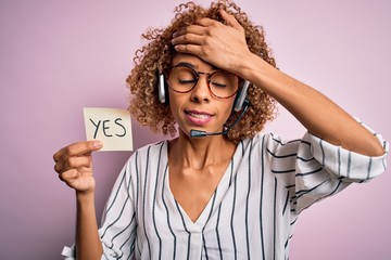 African american call center agent woman using headset holding reminder with yes message stressed...