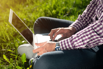 Fototapeta na wymiar vertical shot Young Caucasian man sitting under a tree, typing on a laptop.