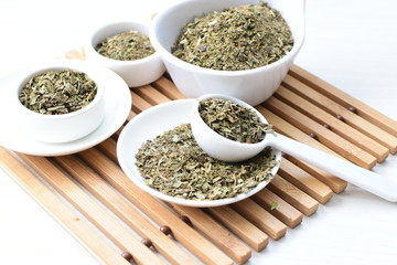 Chopped dried leaves of basil leaves on white wooden background