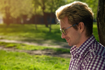 Portrait of a young handsome fair-haired man on a sunny day on a green background with summer grass.