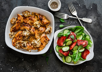 Mustard baked chicken fillet with cauliflower and fresh vegetable salad on a dark background, top view