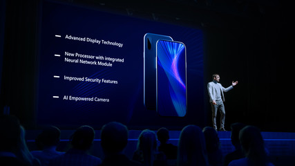 Live Event with Brand New Products Reveal: Keynote Speaker Presents Smartphone Device to Audience. Movie Theater Screen Shows Mock-up Touch Screen Phone with High-Tech Features and Top Highlights - obrazy, fototapety, plakaty