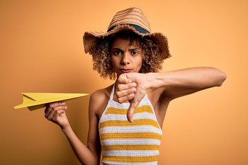 African american tourist woman with curly on vacation wearing summer hat holding paper plane with...