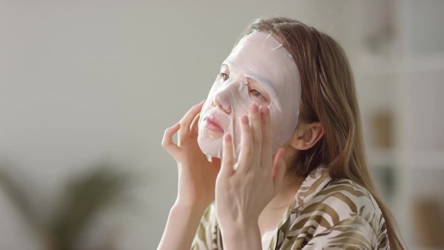  Slowmo of young woman in pajama applying moisturizing sheet face mask in morning