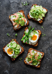 Sandwiches with cream cheese, egg, asparagus, avocado, cucumber, shrimp, micro greens on a dark background, top view. Delicious snack, tapas, appetizers