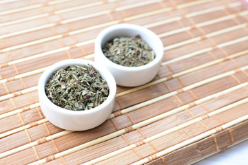 Chopped dried leaves of basil leaves on white wooden background