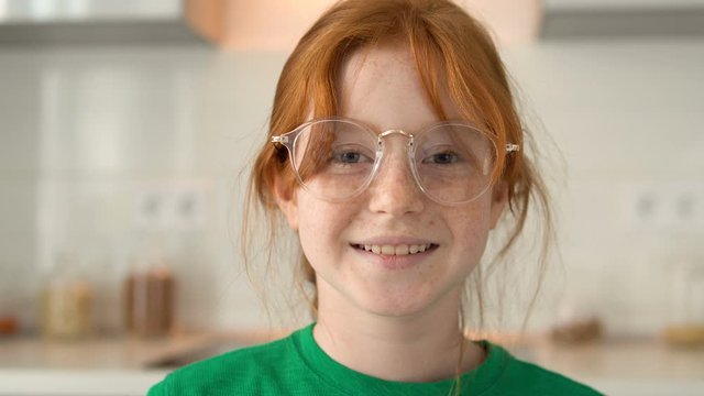 Smiley, freckles face, red-haired girl in eyeglasses looking at camera, giggling