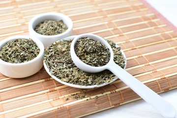 Chopped dried leaves of basil leaves on white wooden background