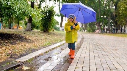 Little boy with umbrella walking at park during rain