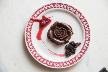 postre de rosa de chocolate negro con frutos rojos y plato blanco con guirnaldas rojas