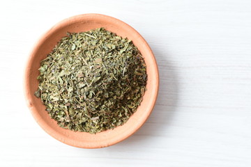 Chopped dried leaves of basil leaves on white wooden background