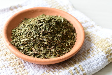 Chopped dried leaves of basil leaves on white wooden background