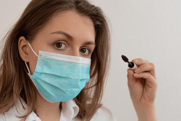 Woman in a medical mask does makeup, mascaras her eyes. The face of a young beautiful woman in a stylish mask