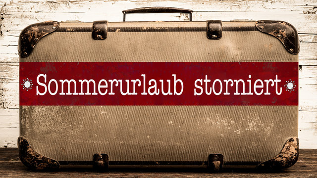 CORONA-REISEWARNUNG - Alter rustikaler vintage Koffer mit rotem Banner und weißem Schriftzug "SOMMERURLAUB STORNIERT"