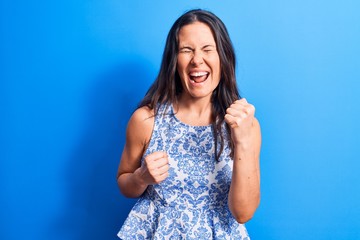 Young beautiful brunette woman wearing casual sleeveless t-shirt over blue background celebrating...