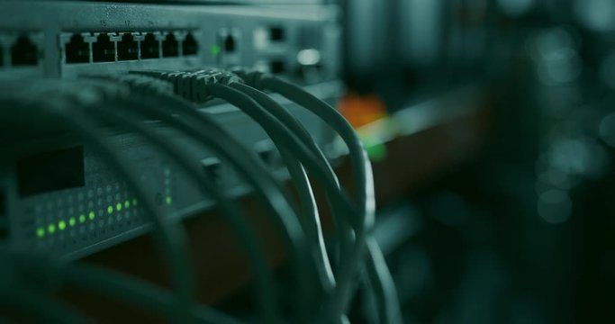 Networking hardware with attached RJ45 ethernet cables working in a dark datacenter room. New activity lights start blinking as new device is being attached to the network
