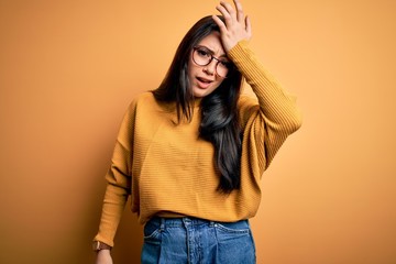 Young brunette woman wearing glasses and casual sweater over yellow isolated background surprised...