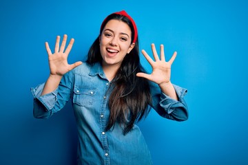 Young brunette woman wearing casual denim shirt over blue isolated background showing and pointing up with fingers number ten while smiling confident and happy.