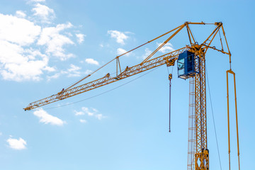 Industrial construction building crane. Yellow mobile rotary crane with a cabin of the operator against a blue sky. Large tall machine used for moving heavy objects. 